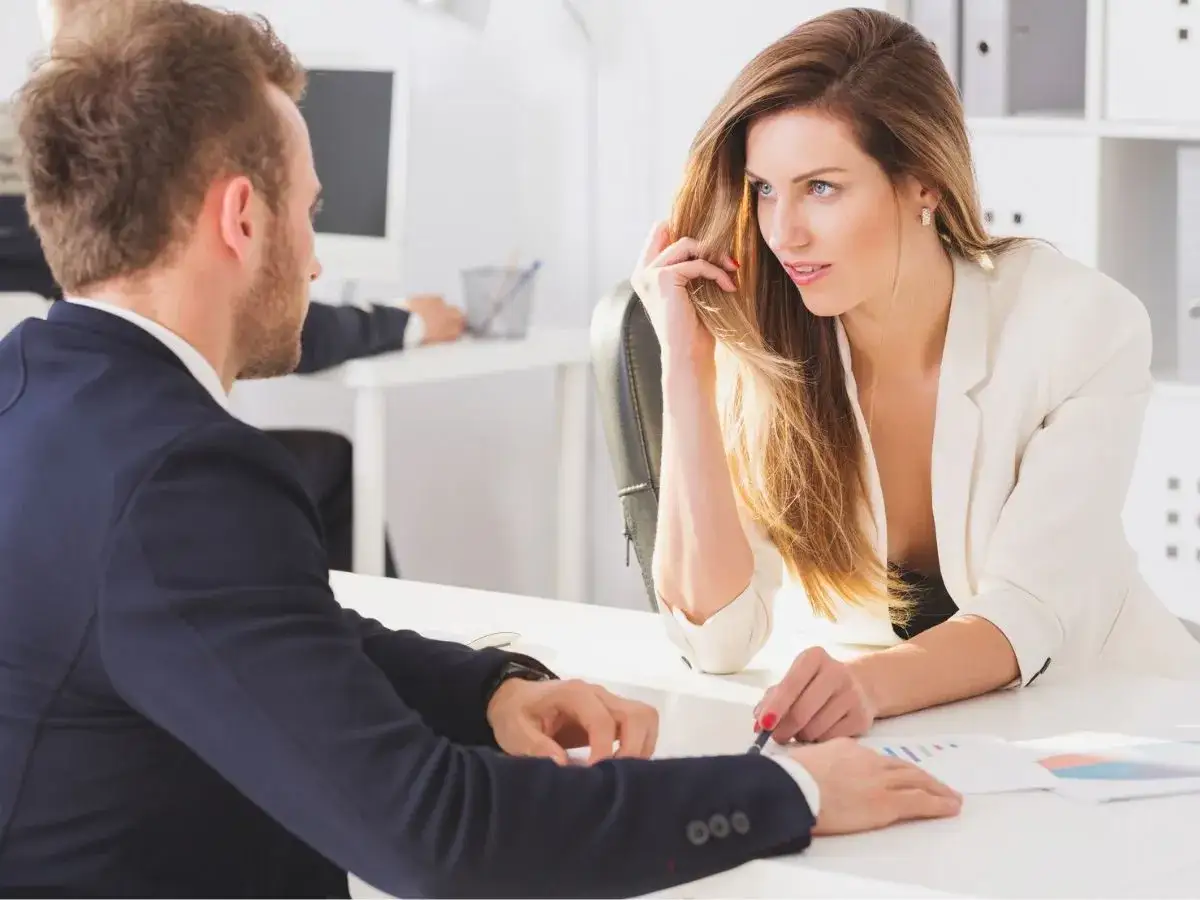 Kobieta w białej marynarce i mężczyzna w granatowej rozmawiają przy biurku. Czy to zakochany szef objawy?