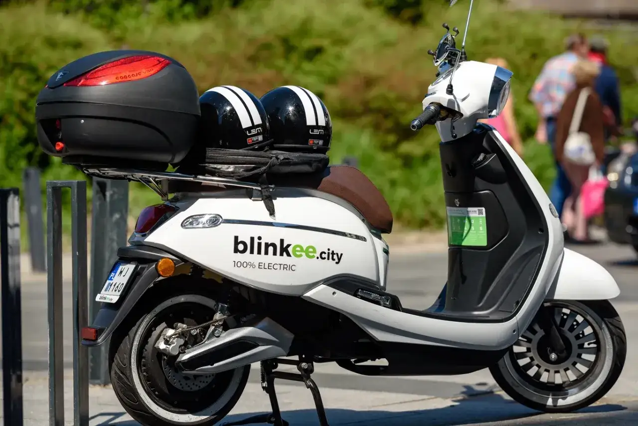 Biały skuter elektryczny z dwoma kaskami. Idealny dla każdego, kto szuka ekologicznego sposobu na poruszanie się po mieście.