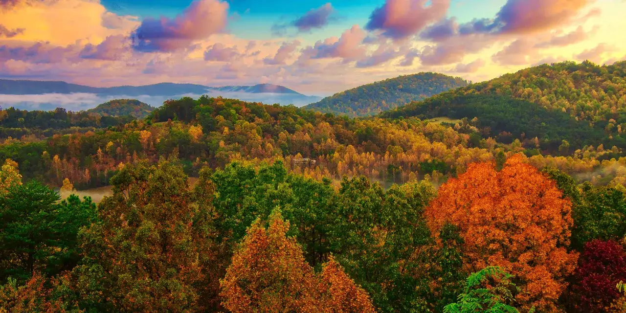 Jesienne góry w pełni kolorów. Mgła unosi się między drzewami, a niebo mieni się odcieniami pomarańczy i różu. Idealne miejsce, gdzie w góry jesienią.