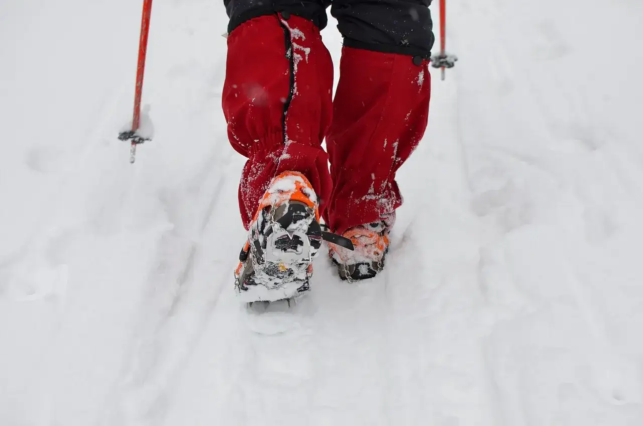 Osoba w czerwonych ochraniaczach i butach z rakami na śnieg stawia kroki w głębokim puchu.