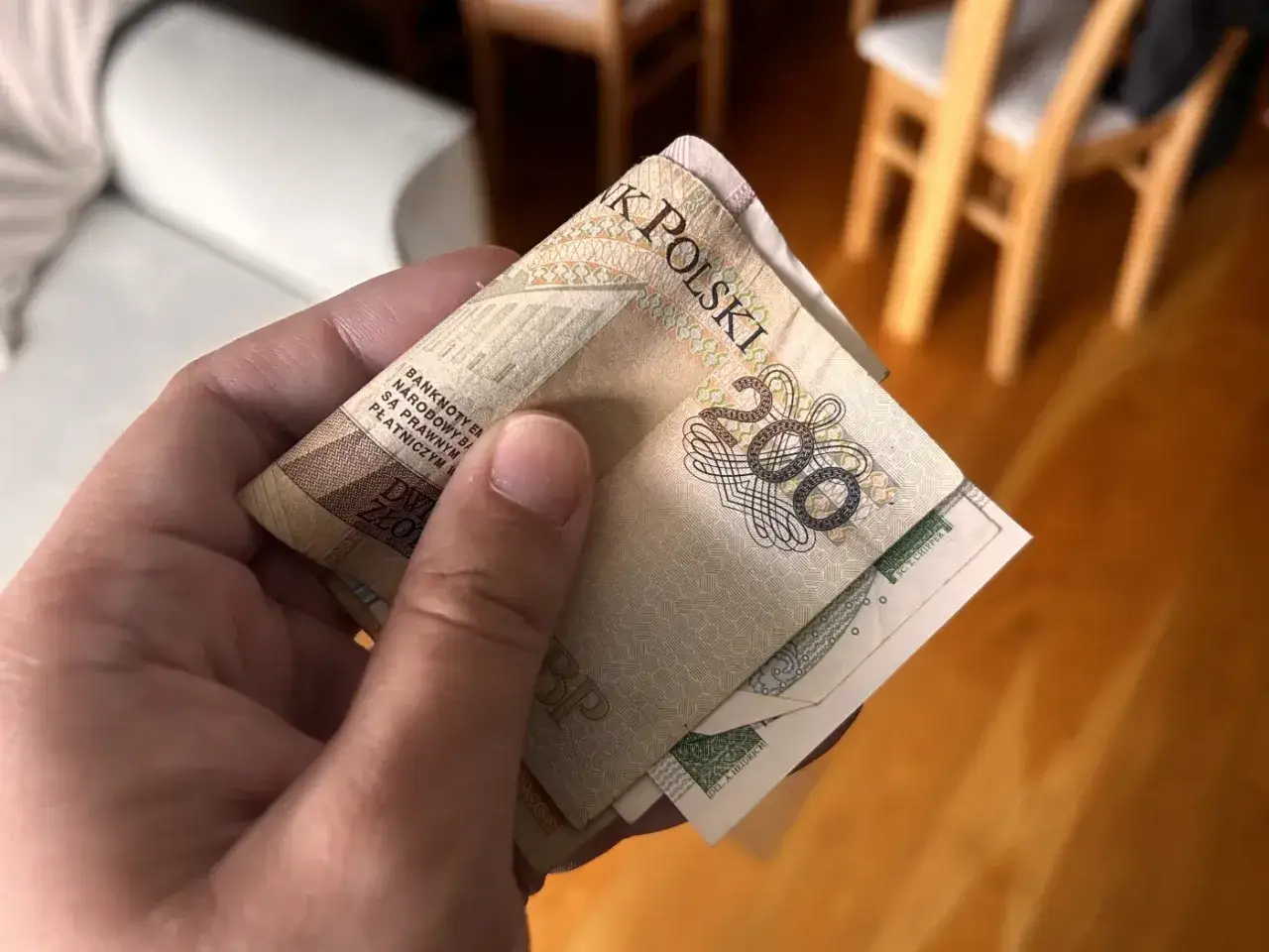 Dłoń trzyma banknot 200 zł. To dobry początek, by dowiedzieć się, jak zostać księgowym i zarządzać finansami.