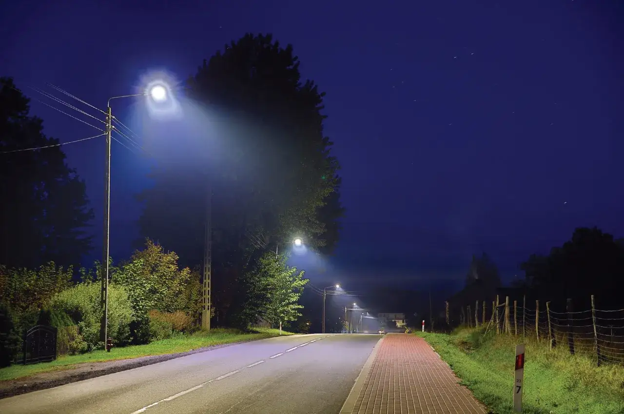 Jasna droga i chodnik oświetlone przez latarnie. Oświetlenie parkingu zapewnia widoczność w nocy.
