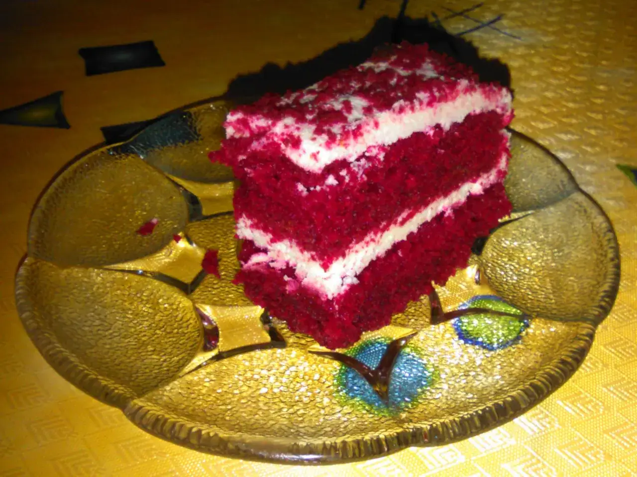 Kawałek ciasta red velvet z kremem na złotej paterze.