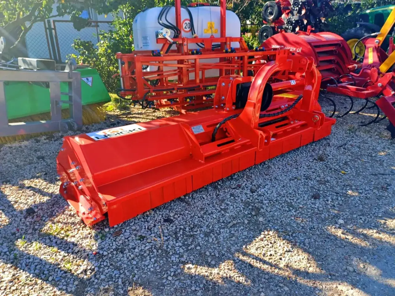 Pomarańczowy mulczer do traktorka, gotowy do pracy w polu. Solidna konstrukcja i logo producenta.