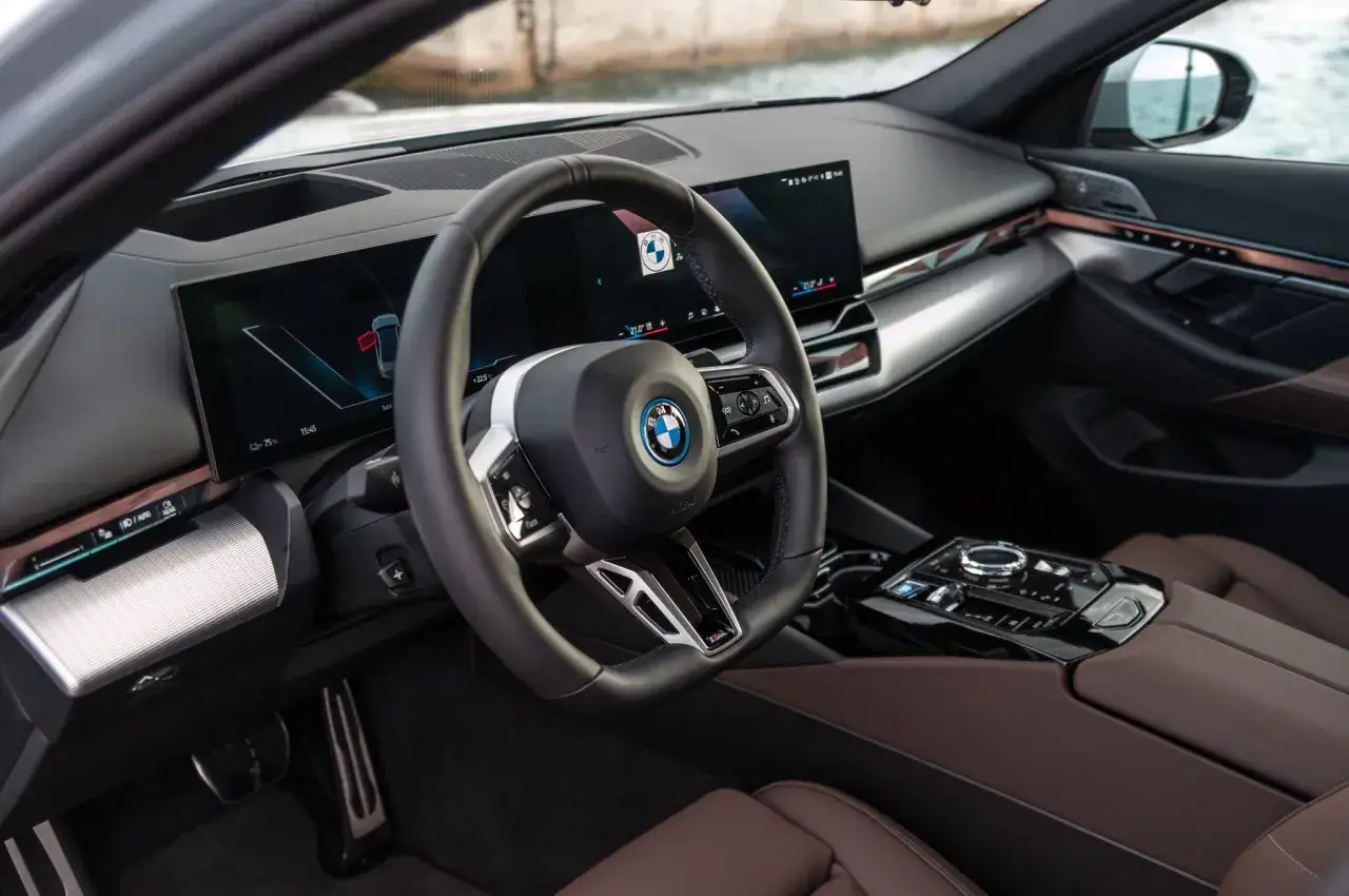 Wnętrze BMW serii 5 z nowoczesnym kokpitem, dużymi ekranami i brązową skórzaną tapicerką.