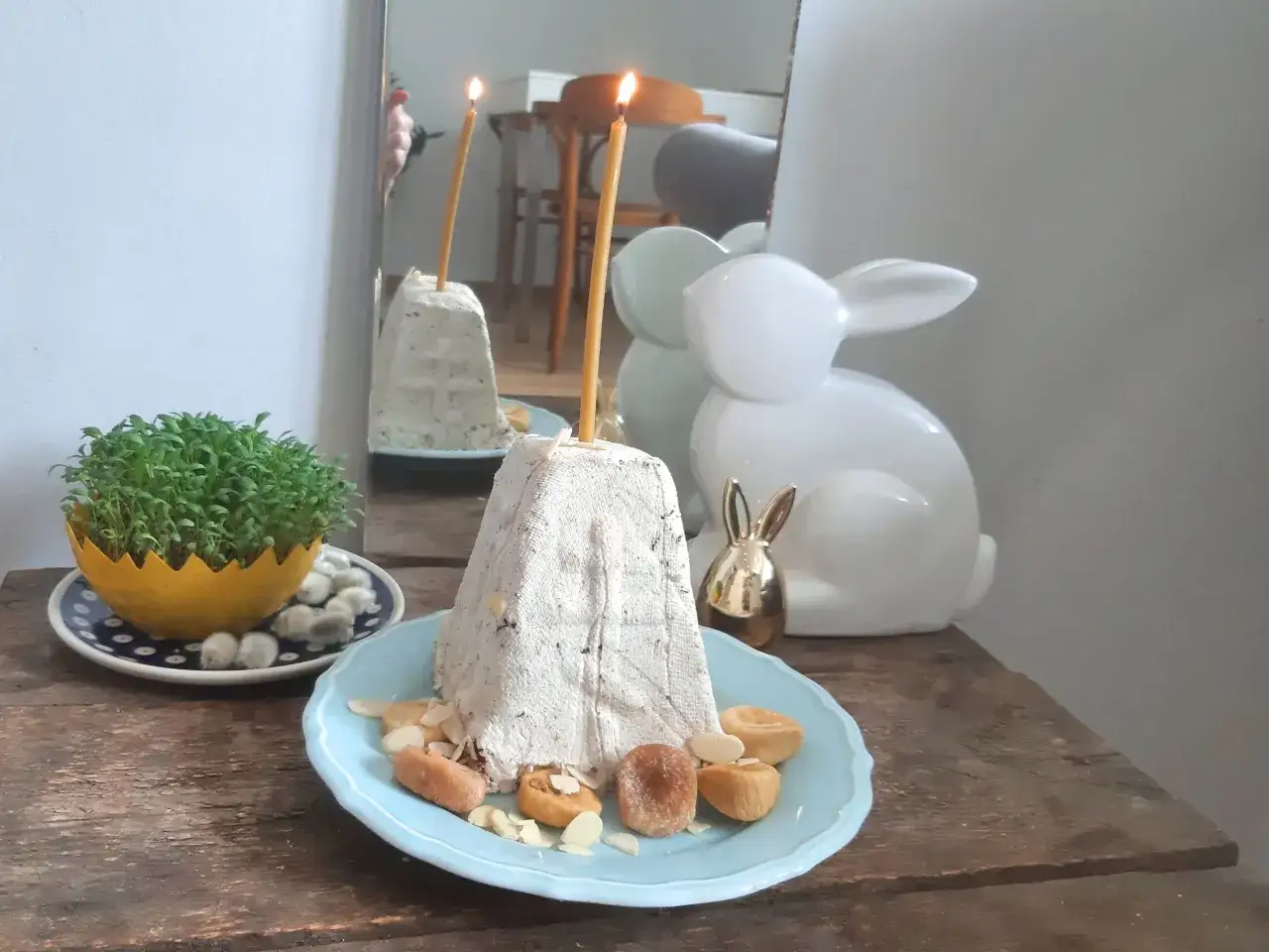 Nowoczesne potrawy wielkanocne: biała pascha z bakaliami i świecami, zielona rzeżucha w ż&oacute;łtej miseczce, zajączek.