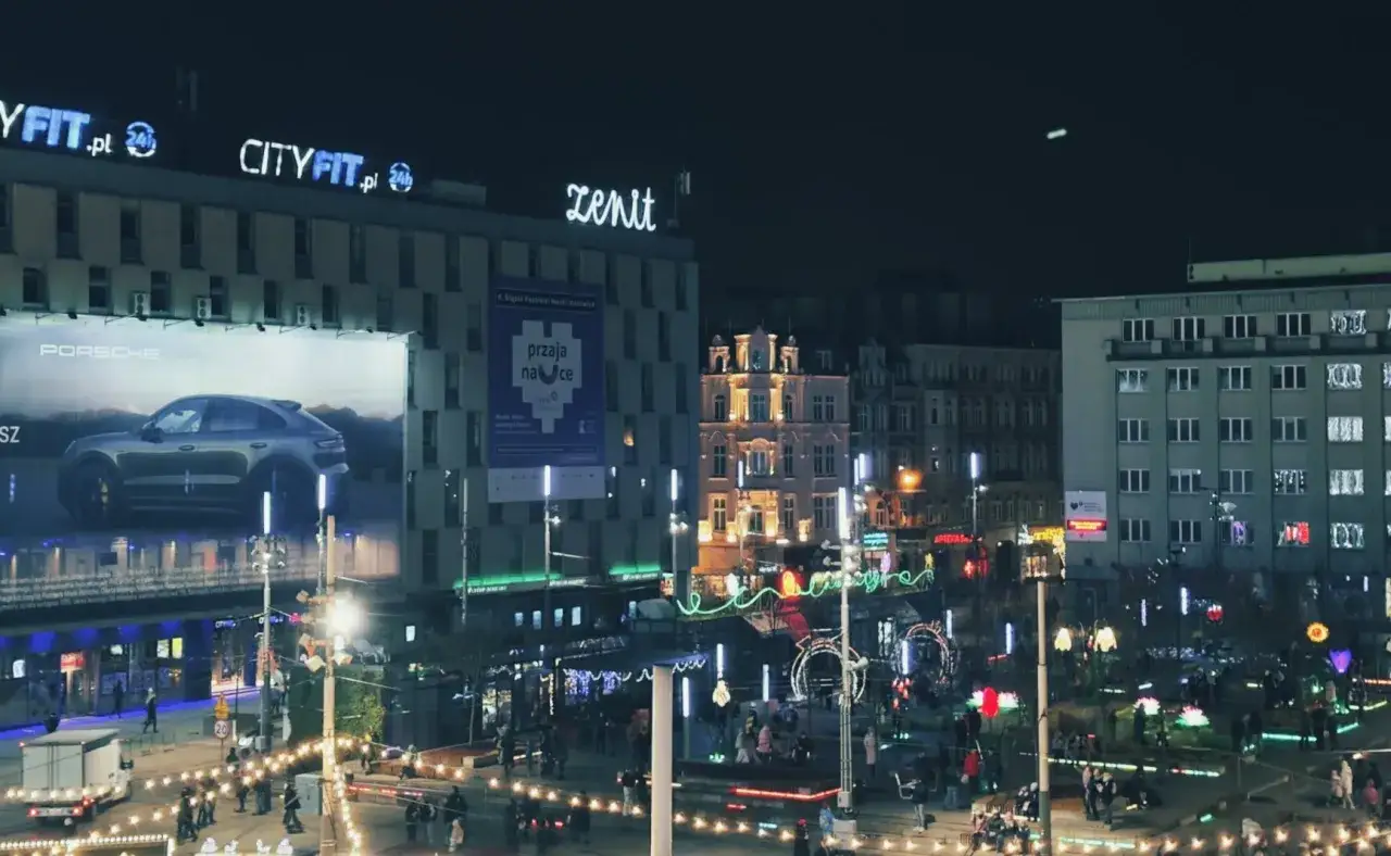 Nocne miasto rozświetlone neonami i ozdobami świątecznymi. Reklama Porsche i budynki Cityfit.pl. Zdjęcie wykonane w trybie nocnym iPhone.