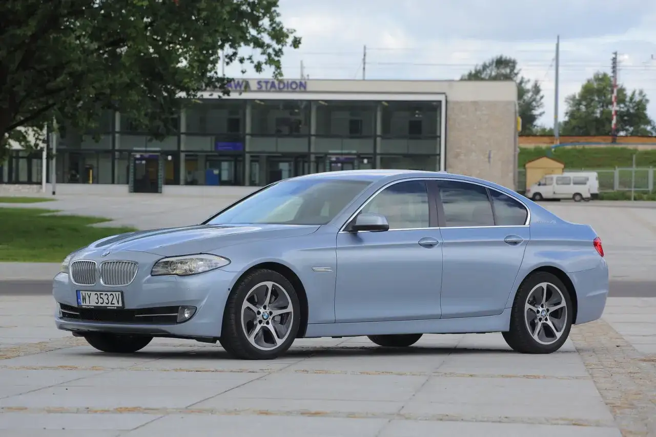 Jasnoniebieskie BMW F10, znane z przestronnego wnętrza, zaparkowane przed stadionem.