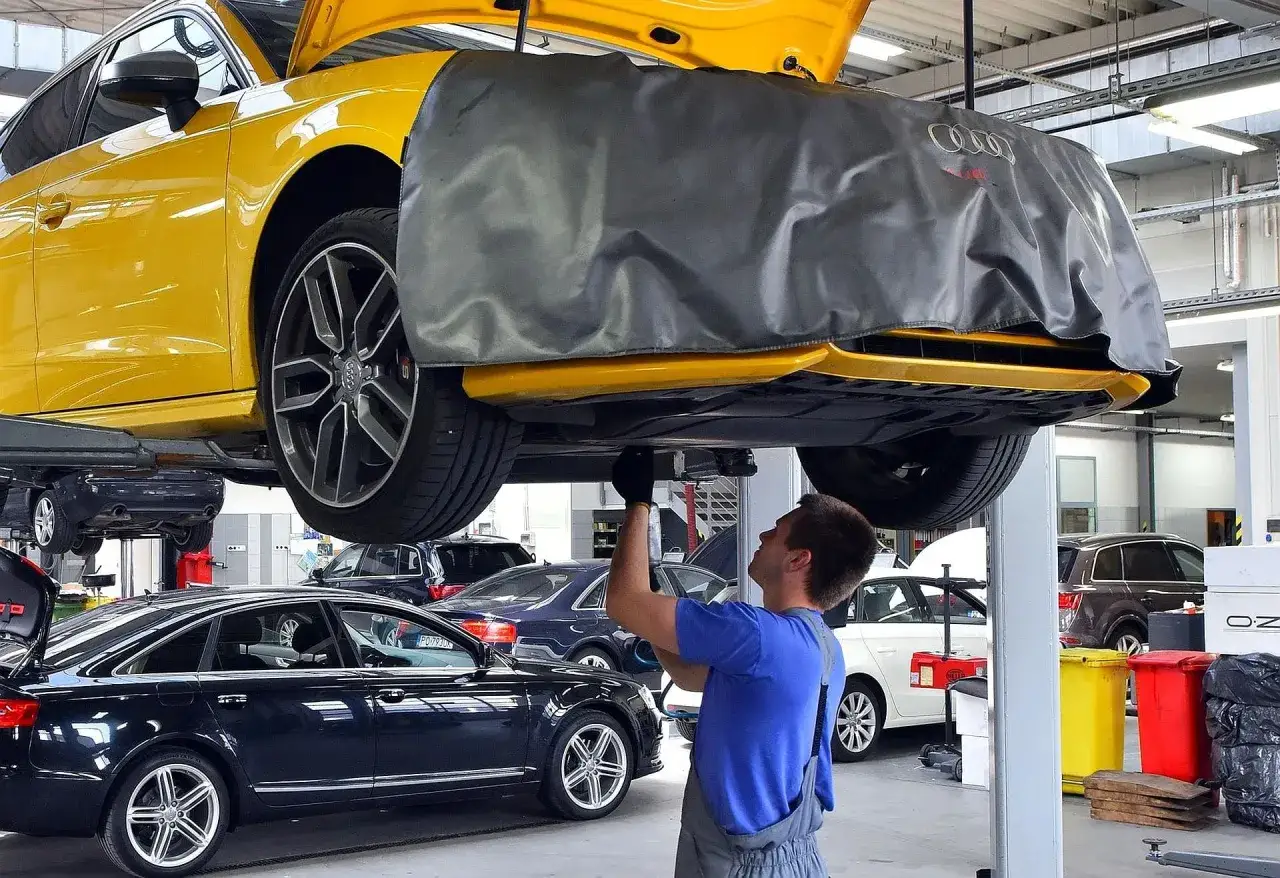 Mechanik pracuje pod żółtym Audi. Zastanawiasz się, ile kosztuje wymiana oleju w samochodzie?