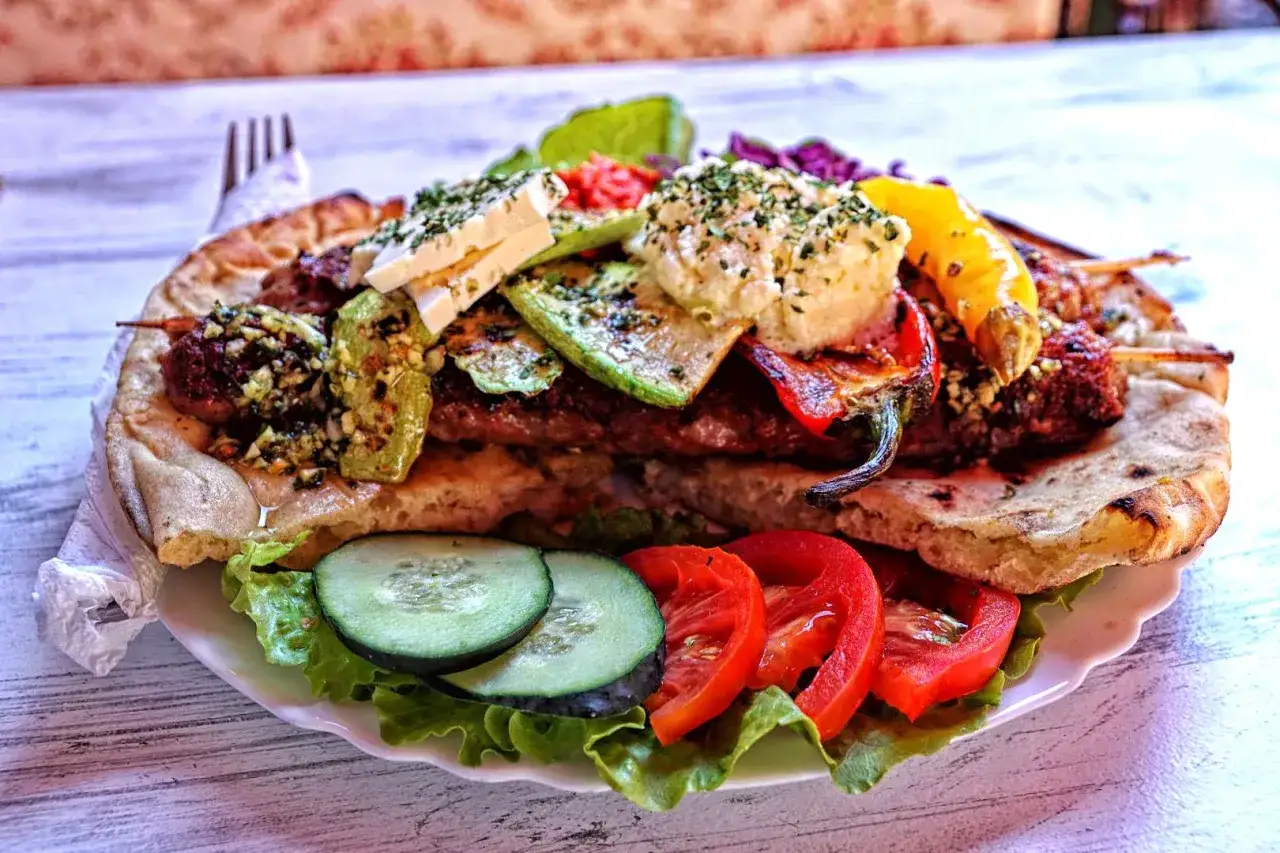 Pyszne danie kuchni bośniackiej: mięso mielone na patyku, grillowane warzywa, ser feta i świeże warzywa na płaskim chlebie.