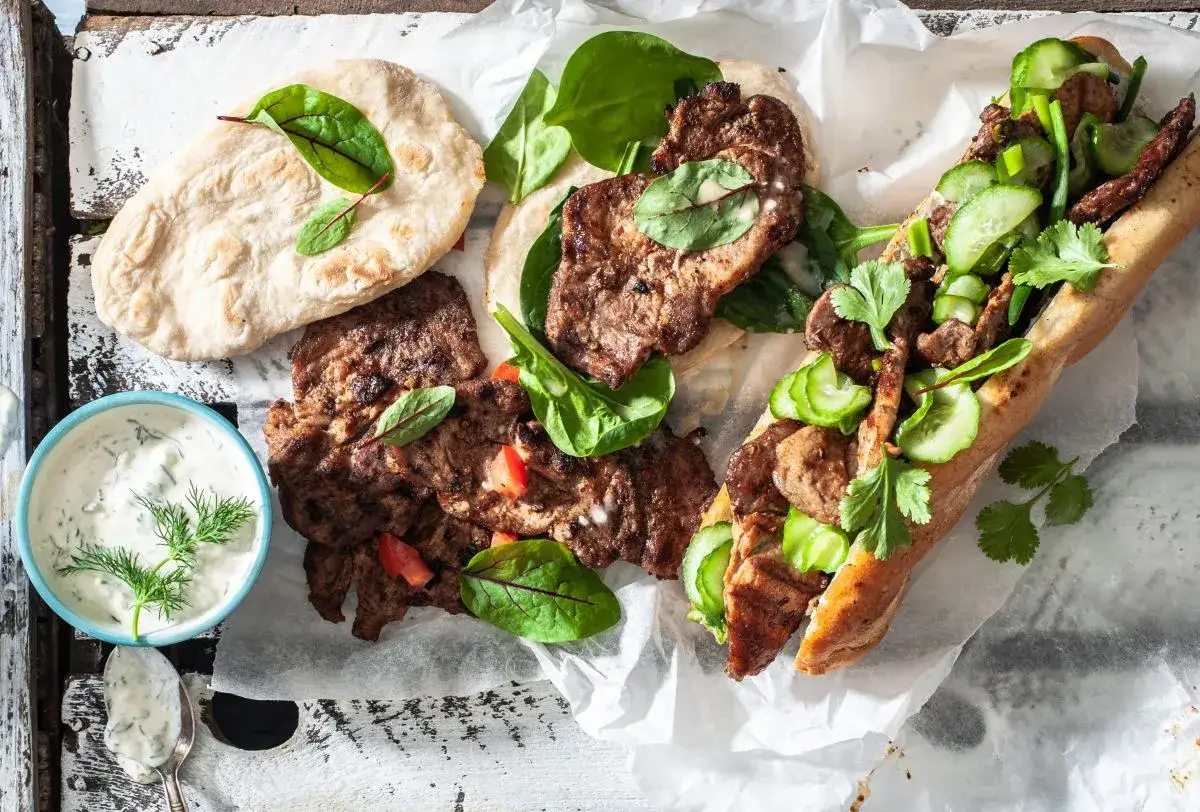 Grillowana karkówka w bułce z ogórkiem i ziołami, obok placki i sos. Idealna na letnie grillowanie, najlepsza marynata do karkówki z grilla!