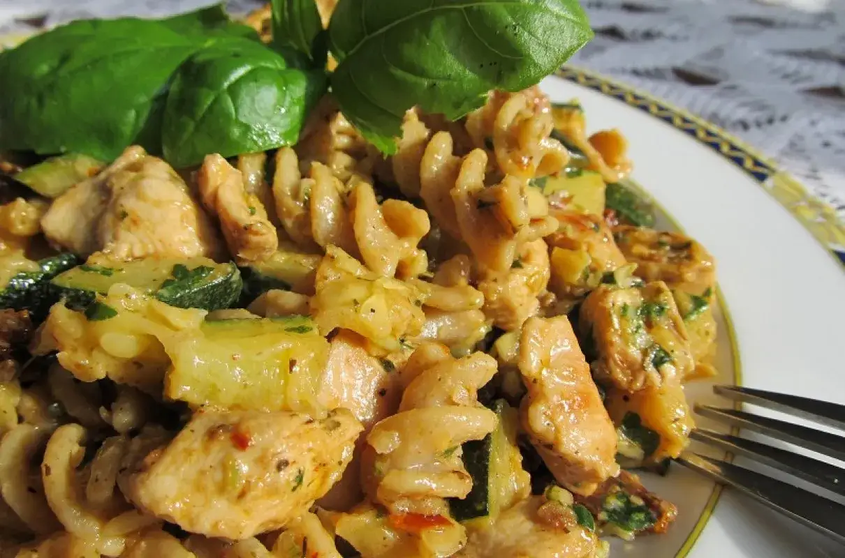 Pyszny makaron z kurczakiem i suszonymi pomidorami, z dodatkiem cukinii i świeżej bazylii.