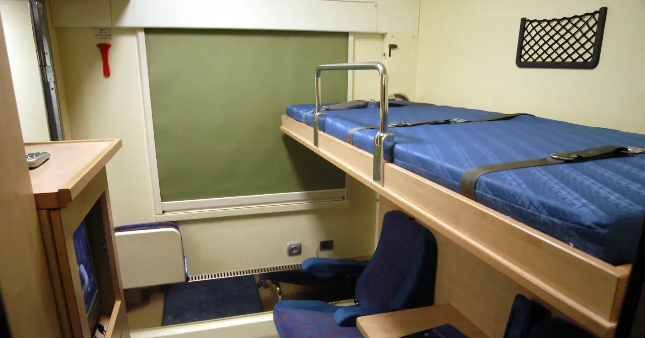 Wnętrze wagonu sypialnego Pendolino z niebieskimi materacami na piętrowych łóżkach i siedzeniami.
