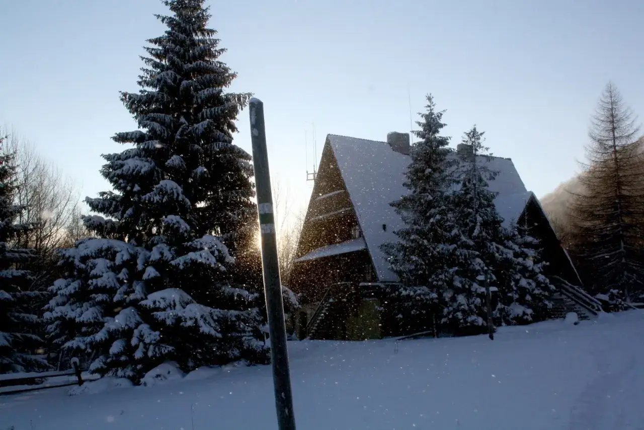 Zimowy krajobraz z zasypaną śniegiem bac&oacute;wką Mała Rawka. Słońce przebija się przez padający śnieg, tworząc magiczny widok.