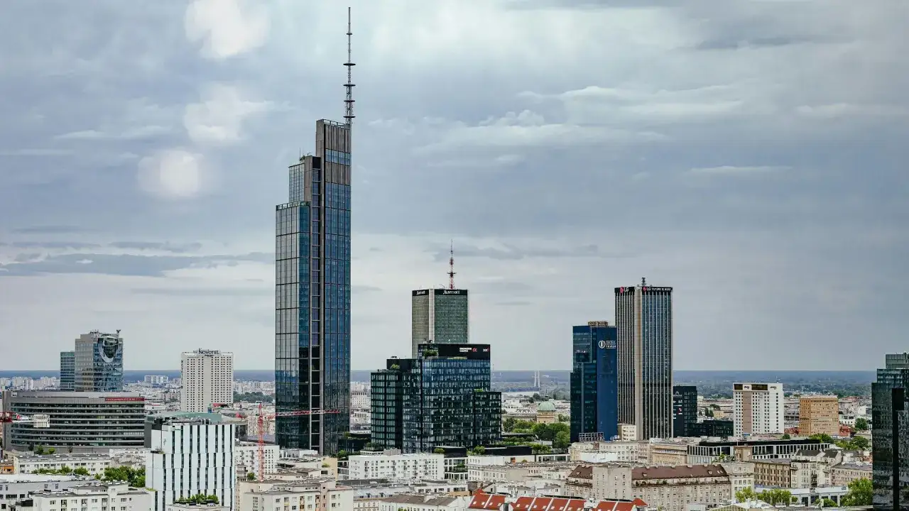 Warszawski krajobraz z wieżowcami, w tym najwyższy budynek w Polsce, na tle pochmurnego nieba.