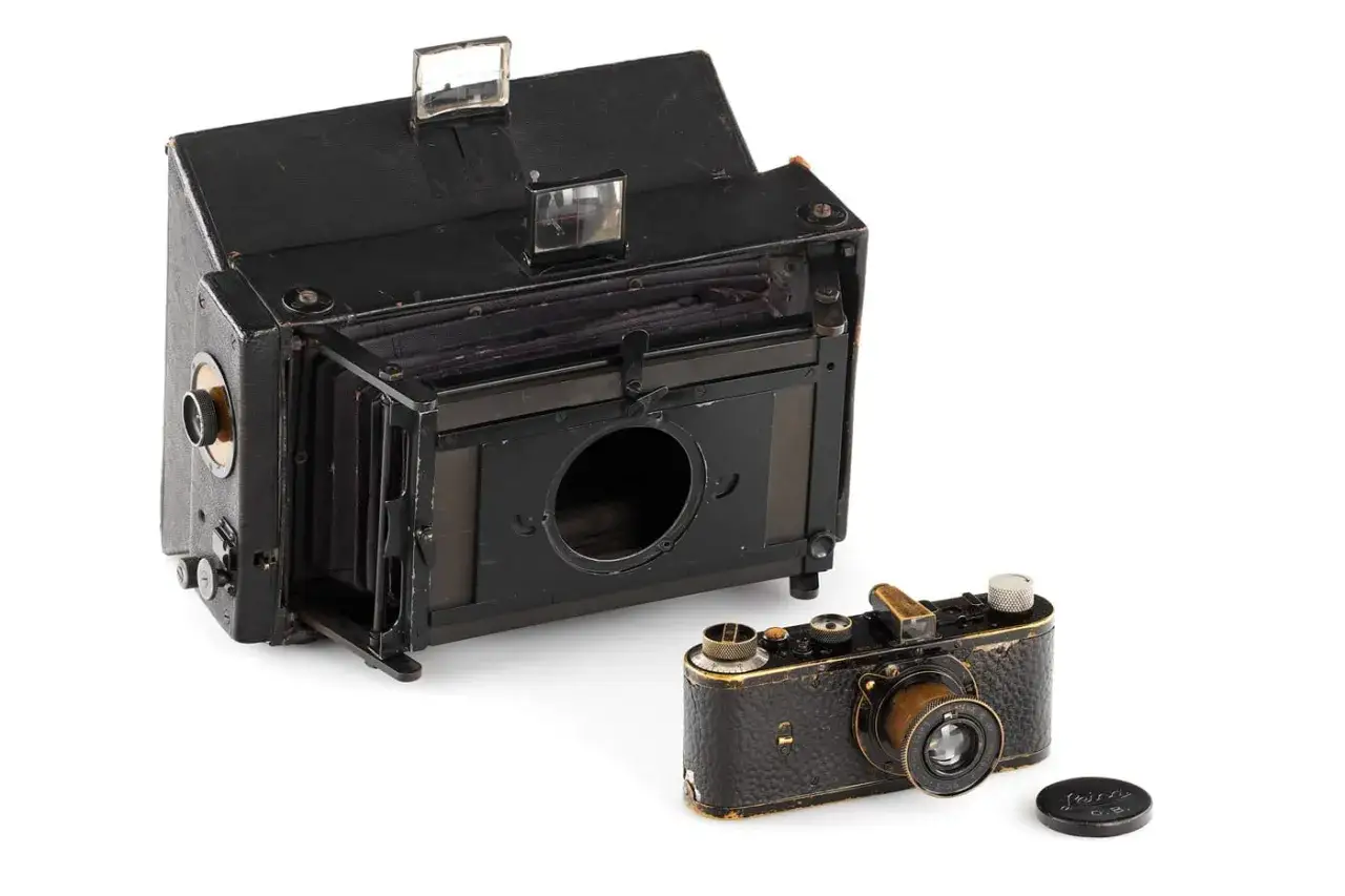 Dwa zabytkowe aparaty fotograficzne, jeden duży harmonijkowy, drugi mały Leica, być może najdroższy aparat fotograficzny w historii.
