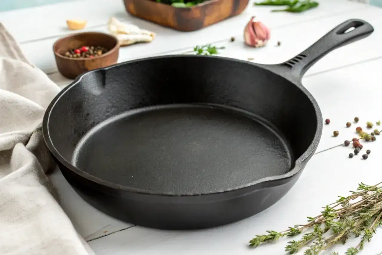 Czarna, żeliwna patelnia na białym stole, otoczona przyprawami. Dowiedz się, jakich patelni należy unikać, by gotować zdrowo.