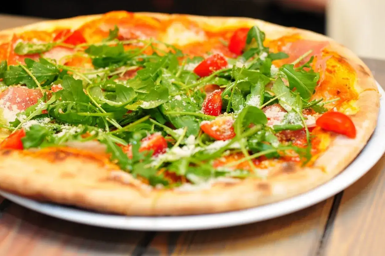 Domowa pizza z rukolą i pomidorkami, posypana parmezanem. Zastanawiasz się, ile kcal ma domowa pizza?