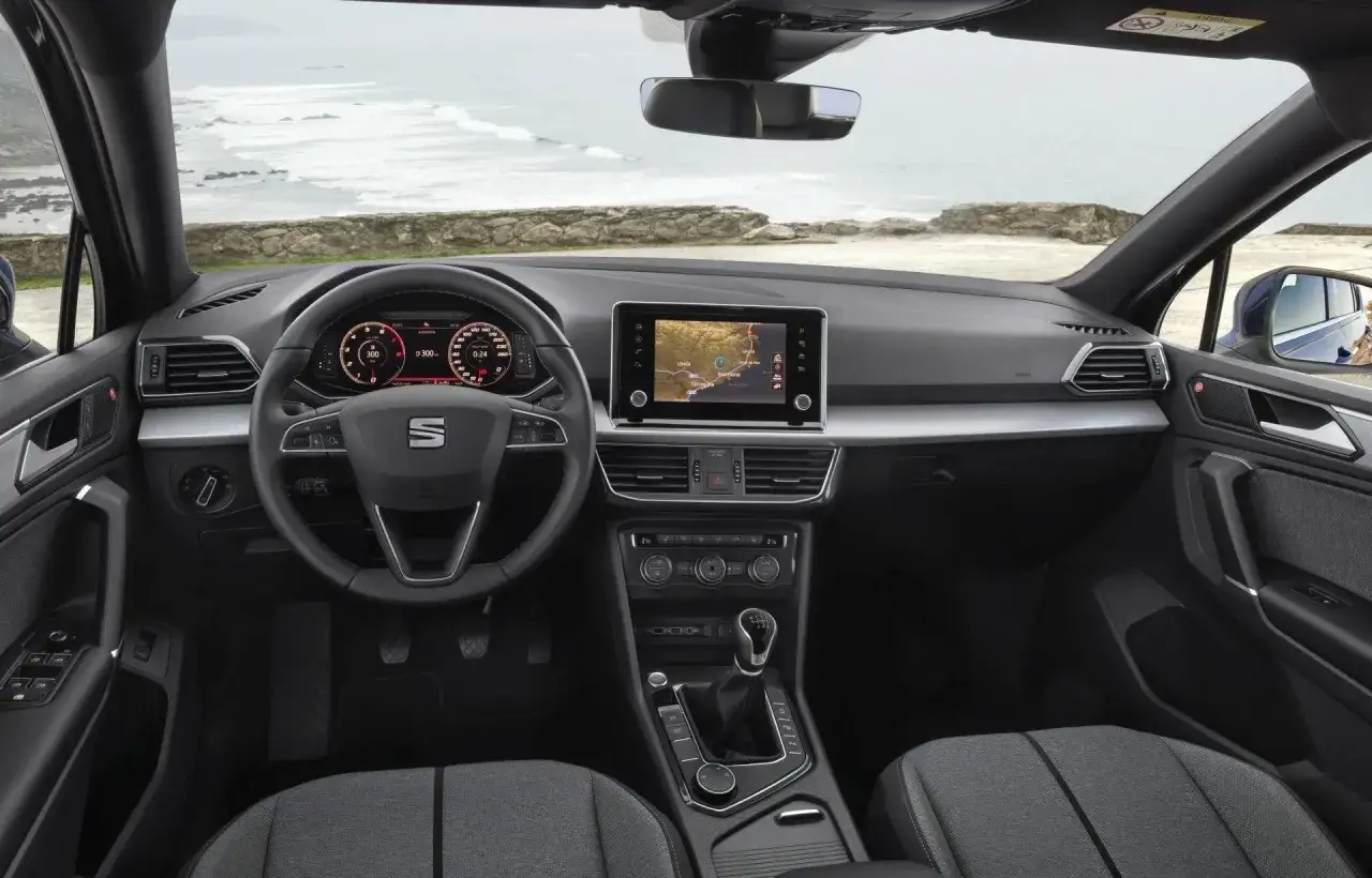 Wnętrze Seat Tarraco z widokiem na morze. Cyfrowe zegary, ekran nawigacji i kierownica.
