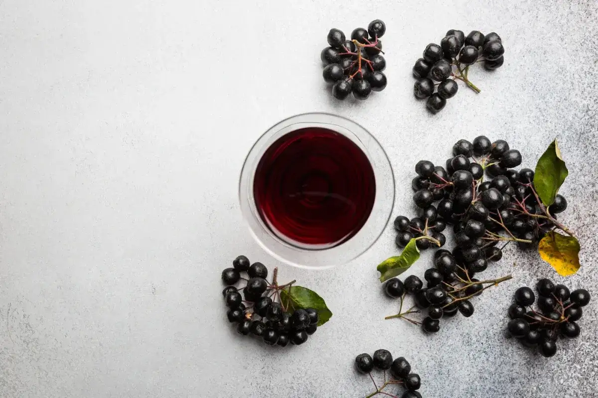 Szklanka z ciemnym sokiem z aronii i kiście świeżych owoców. Idealne do mrożenia aronii na zimę.