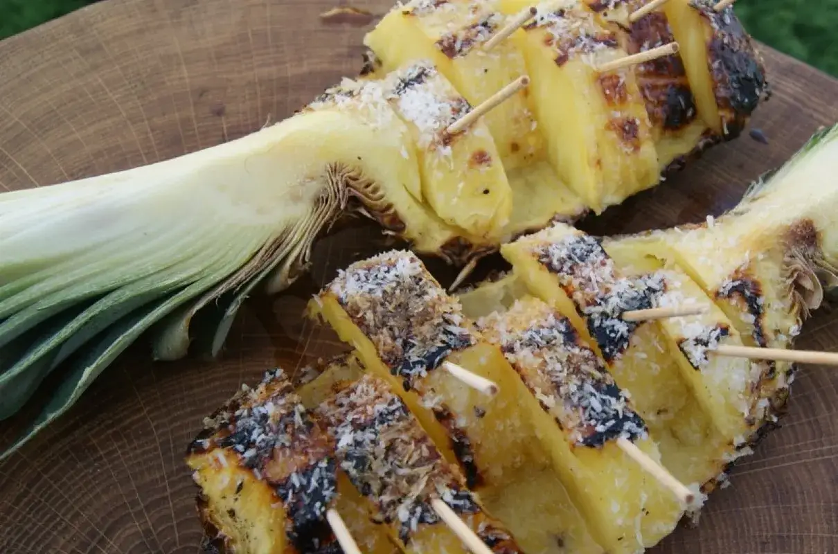 Słodki, grillowany ananas z wi&oacute;rkami kokosowymi, nabity na patyczki, czeka na podanie.
