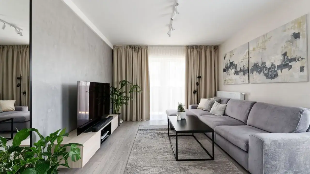 Nowoczesna aranżacja ściany za kanapą: szara sofa, beton architektoniczny, obrazy i rośliny tworzą przytulną przestrzeń.