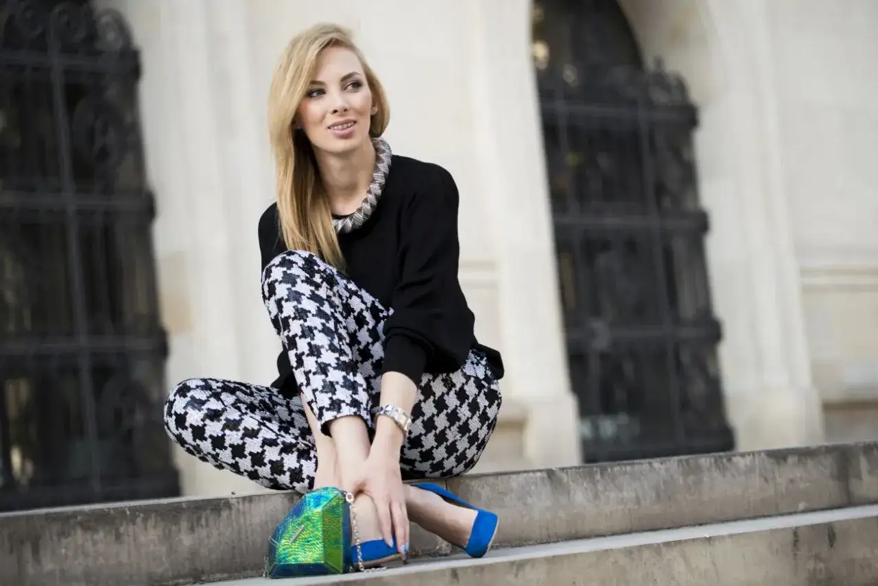 Elegancka kobieta w spodniach w pepitkę, czarnym swetrze i niebieskich szpilkach. Jej stylizacje z pepitką są odważne i modne.