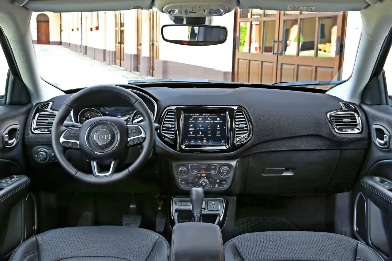 Wnętrze Jeep Compass z kierownicą, ekranem dotykowym i dźwignią zmiany biegów. Widok z perspektywy kierowcy.