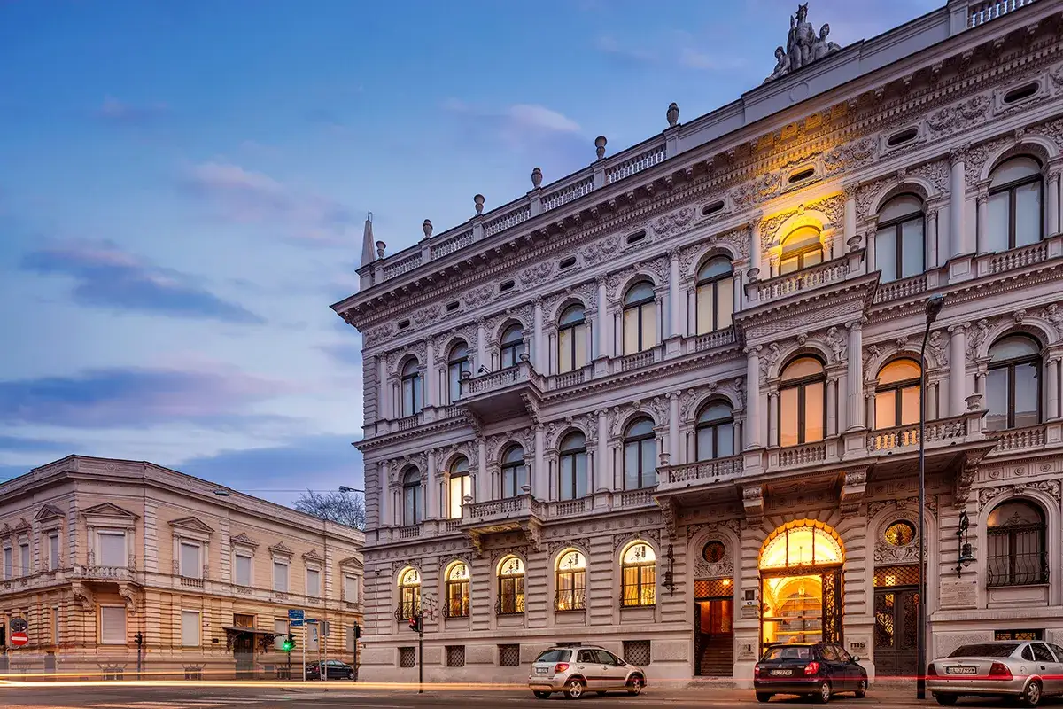Elegancki budynek muzeum sztuki w Łodzi, oświetlony wieczornym światłem, z widocznymi samochodami na ulicy.