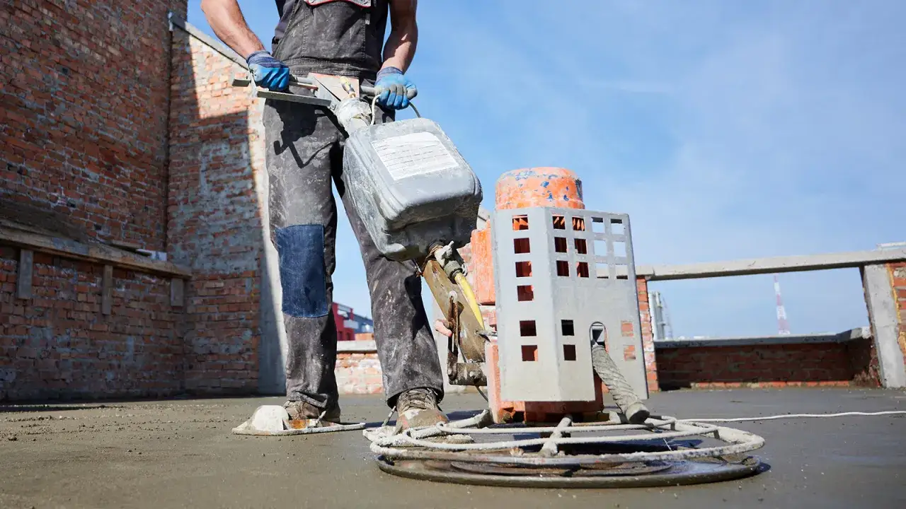 Pracownik wylewa płyn na maszynę do zacierania betonu. Dowiedz się, jak zrobić wylewkę betonową.