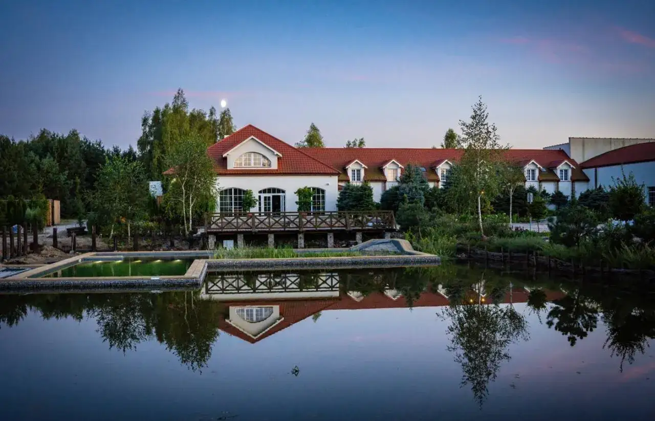 Elegancki hotel spa Warszawa i okolice z basenem i stawem, odbijającymi się w spokojnej wodzie.