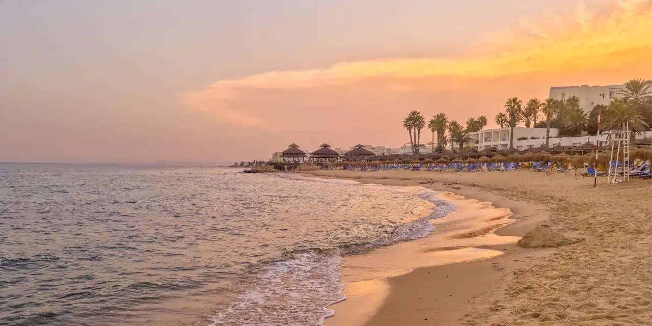 Zachód słońca na plaży w Tunezji. Czy w Tunezji jest drogo? Widok na morze, piasek, leżaki i palmy.