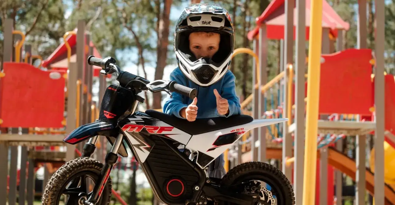 Mały kierowca w kasku z kciukami w górę, gotowy na przygodę na swoim motocyklu.