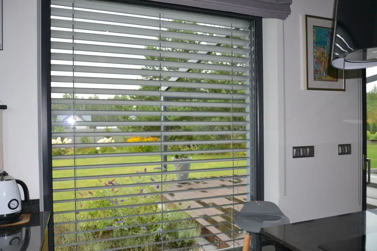Nowoczesne żaluzje fasadowe wewnętrzne z widokiem na zielony ogród.