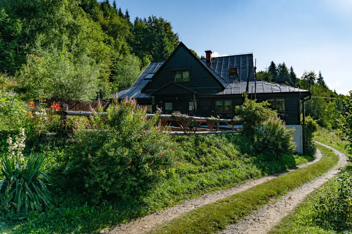 Drewniana bac&oacute;wka pod Bereśnikiem otoczona zielenią. Droga prowadzi do obiektu, gdzie można sprawdzić bac&oacute;wka pod bereśnikiem cennik.