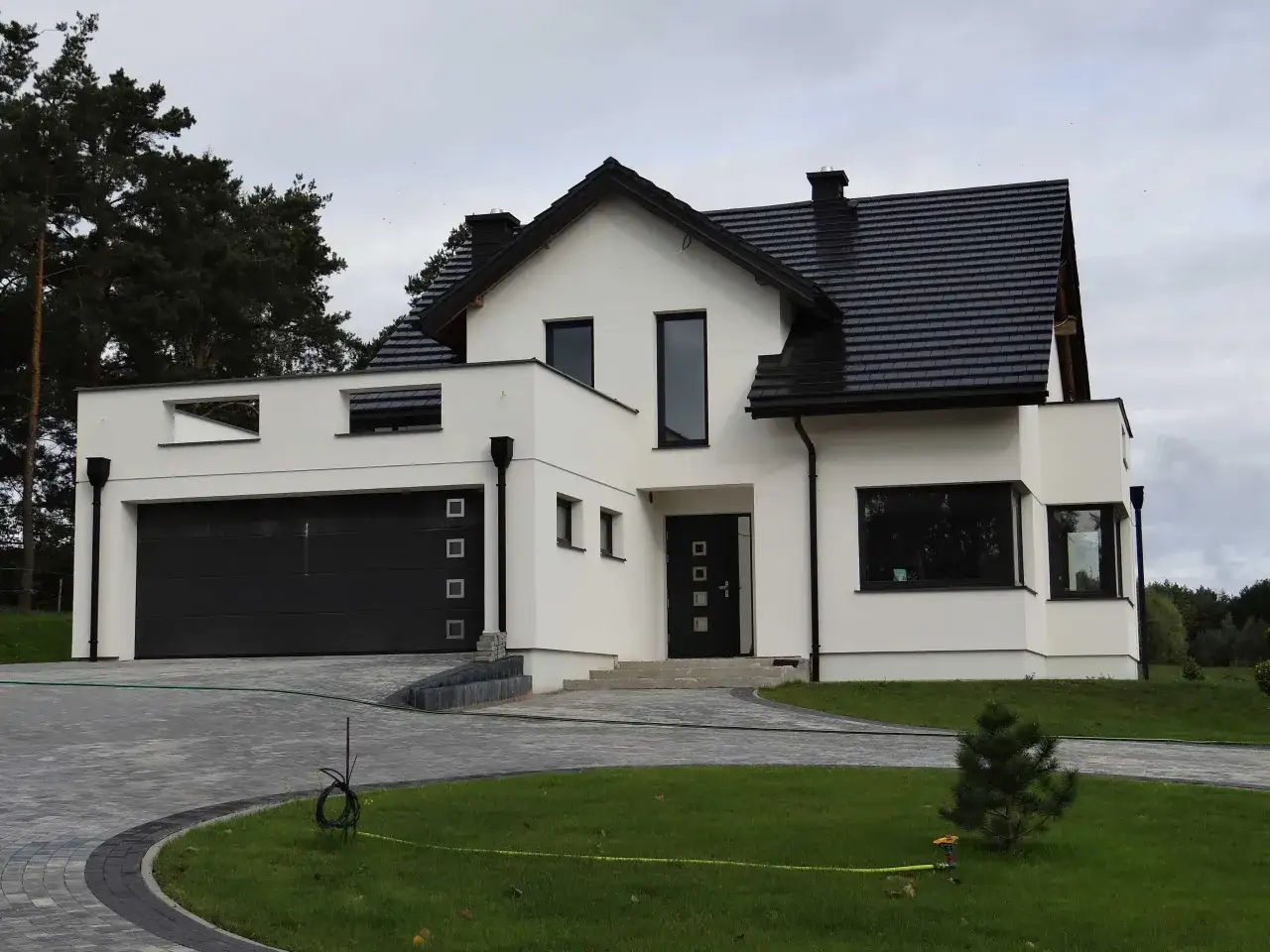 Nowoczesny dom z białymi ścianami, ciemnym, antracytowym dachem i oknami w stylu winchester.