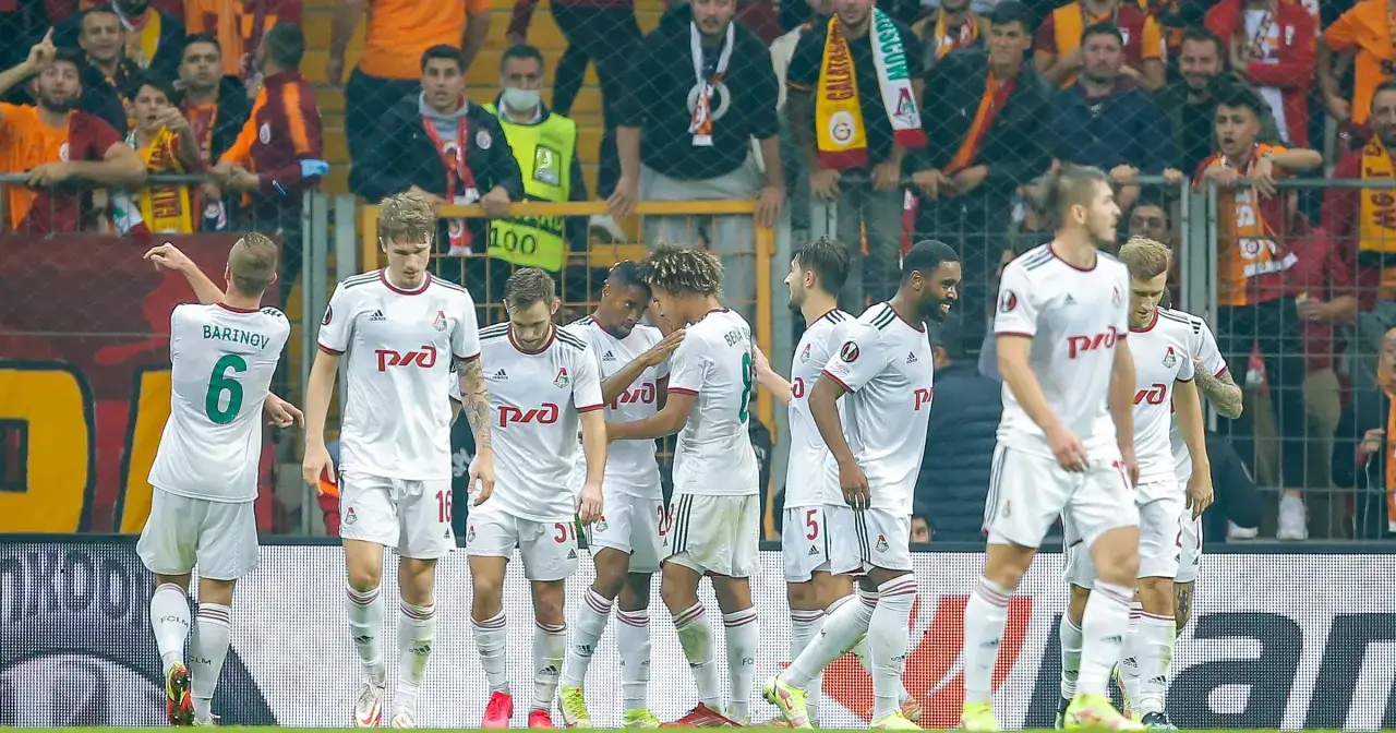 Piłkarze w białych strojach, reprezentujący kluby piłkarskie z Moskwy, świętują bramkę na tle kibiców.