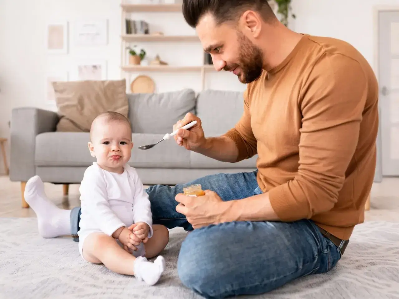 Tata karmi dziecko, co może być częścią jego wniosku o urlop ojcowski. Dziecko ma minę, jakby nie było zachwycone jedzeniem.