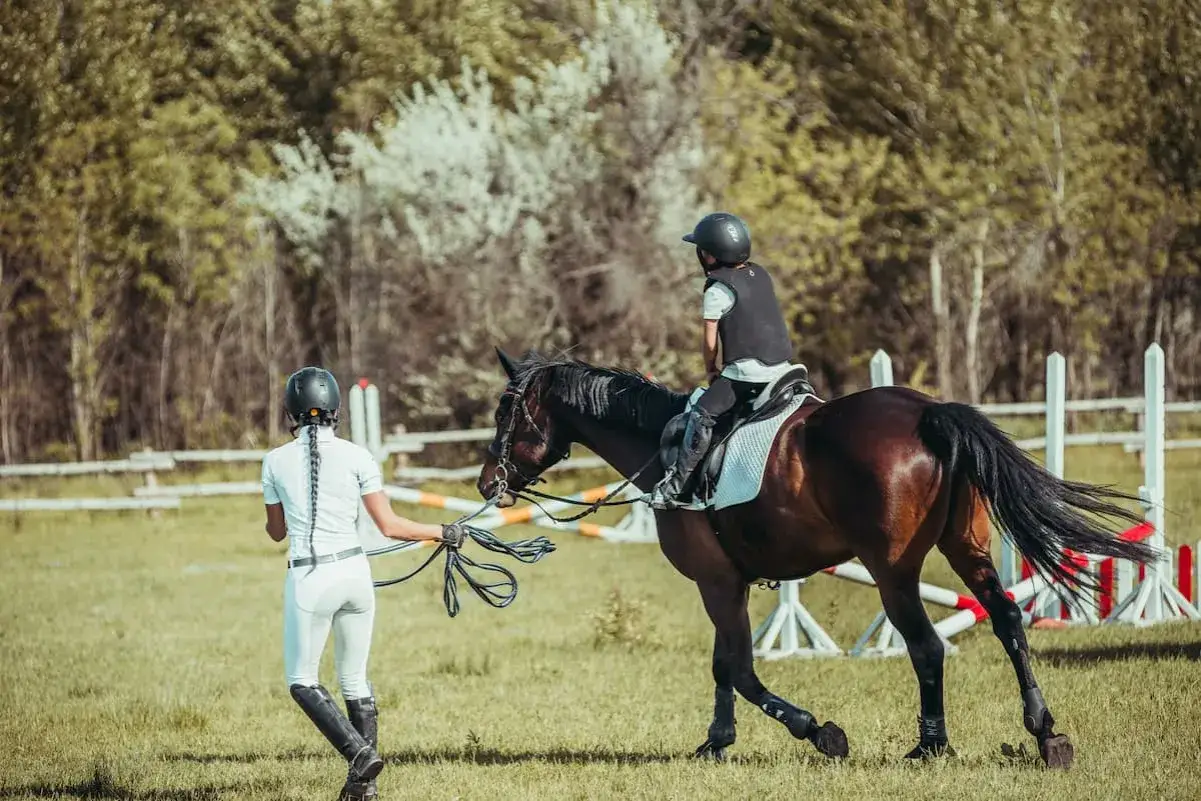 Trening jazdy konnej: młoda jeźdźczyni na koniu, instruktorka prowadzi. Odpowiedź na pytanie, ile trwa nauka jazdy konnej, zależy od wielu czynników.