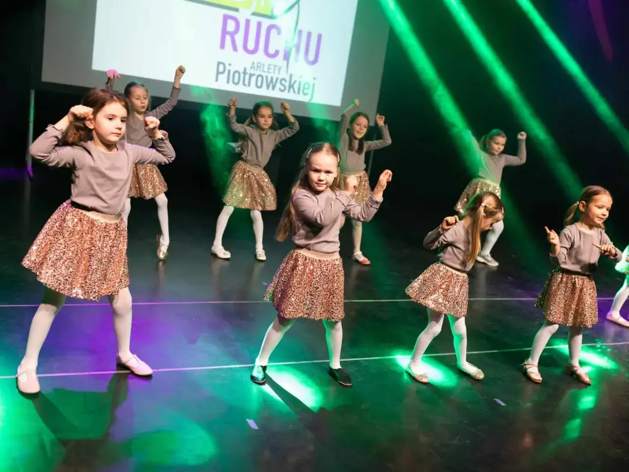 Dziewczynki w błyszczących sp&oacute;dniczkach tańczą na scenie. R&oacute;żne rodzaje tańca dla młodzieży to świetna zabawa i aktywność.