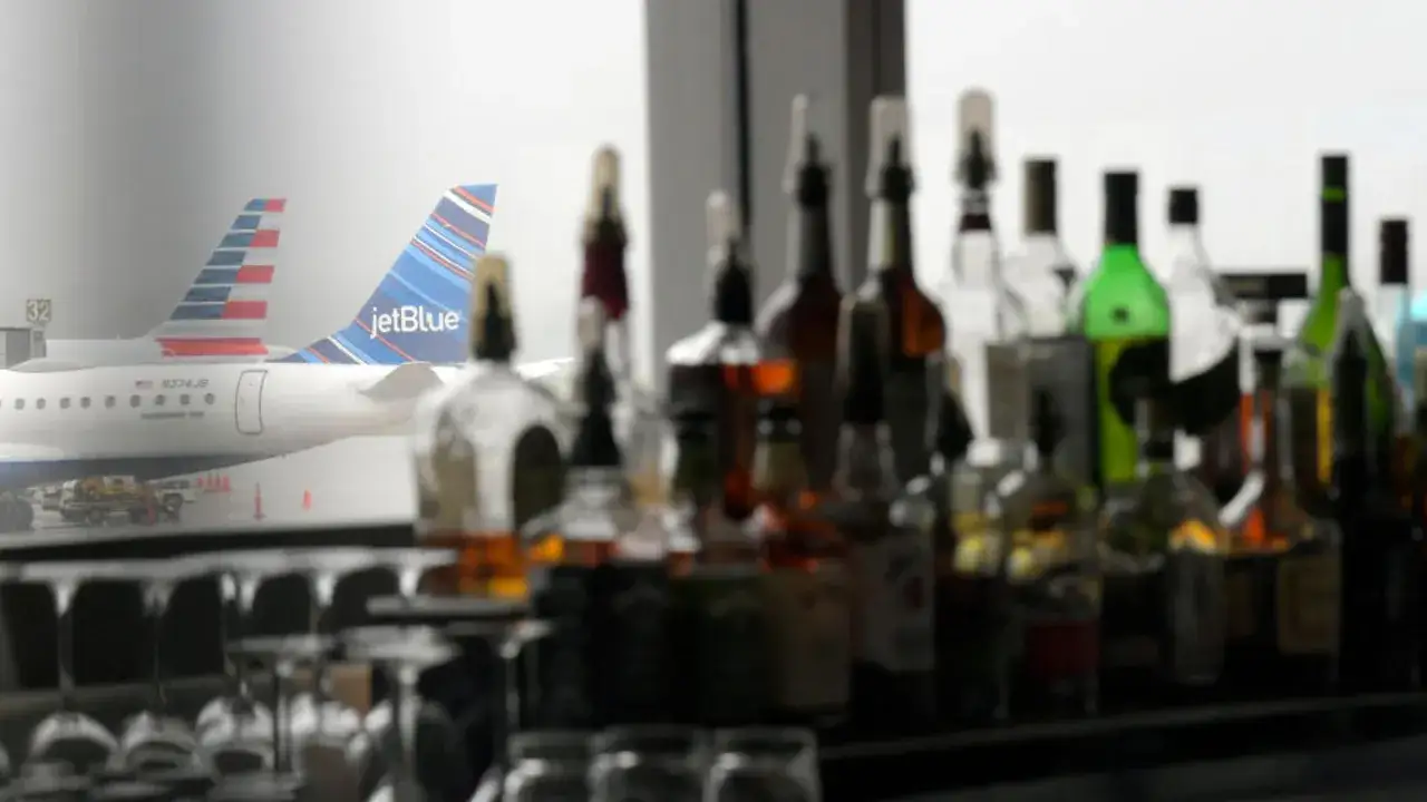 Butelki z alkoholem na pierwszym planie, a w tle samoloty American Airlines i JetBlue. Czy na lotnisku można pić alkohol?