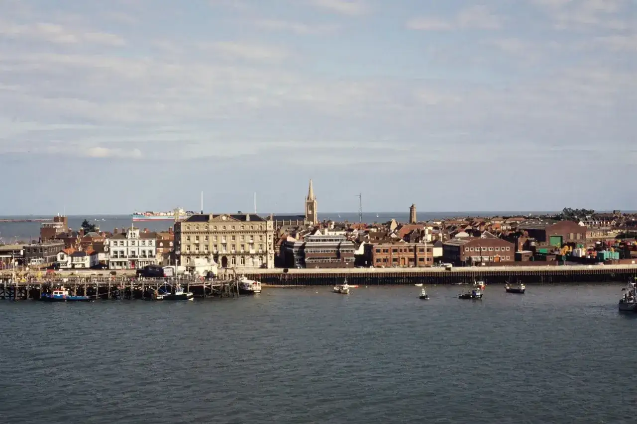 Widok na port w Harwich z promem Hoek van Holland. Widać budynki portowe, molo i kilka statków na wodzie.