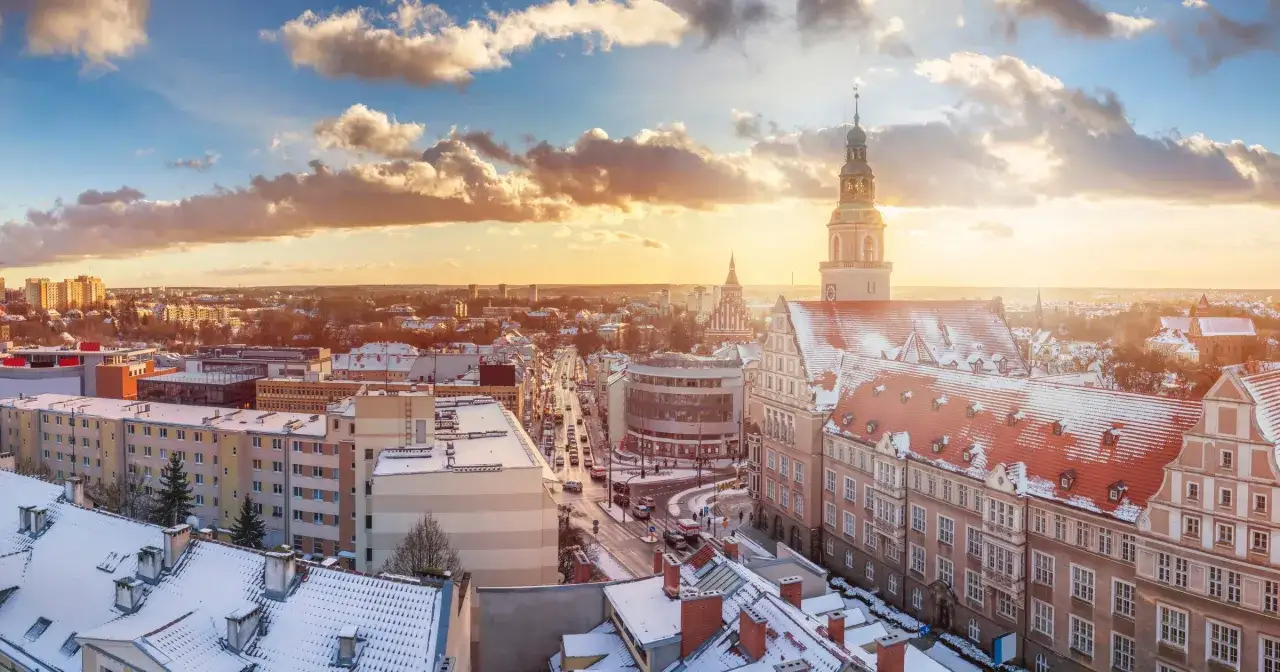 Zachód słońca nad Olsztynem zimą. Warto zobaczyć w Olsztynie piękne kamienice i wieżę ratuszową ośnieżone śniegiem.