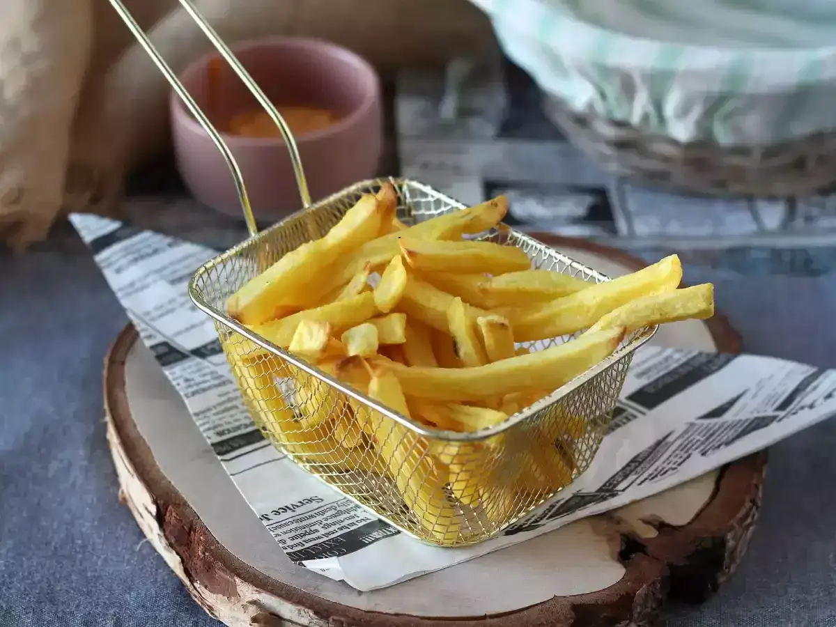 Złociste, chrupiące frytki z mrożonki w koszyku. Idealne do airfryera, by dowiedzieć się, ile smażyć mrożone frytki w airfryer.