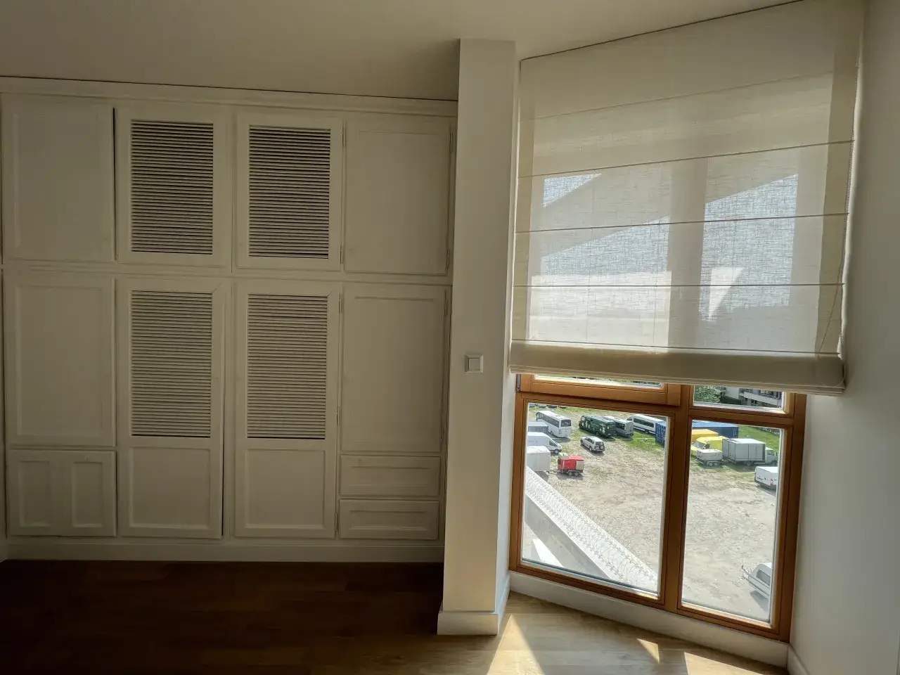 Jasne, oto propozycja:

Zastanawiasz się, jak zrobić rolety rzymskie? Wnętrze z białymi szafami i oknem z jasną roletą rzymską.