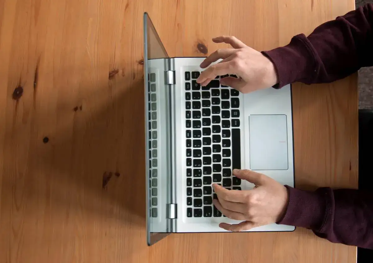 Dłonie na klawiaturze laptopa, pokazujące, jak włączyć dźwięk w laptopie na klawiaturze.