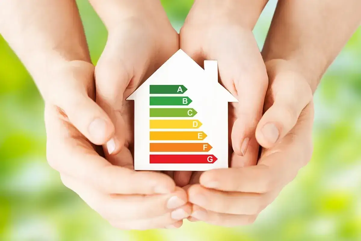 Dłonie trzymają model domu z etykietą energetyczną. Zastanawiasz się, ile prądu zużywa klimatyzator? Ta skala pomoże Ci wybrać energooszczędny model.