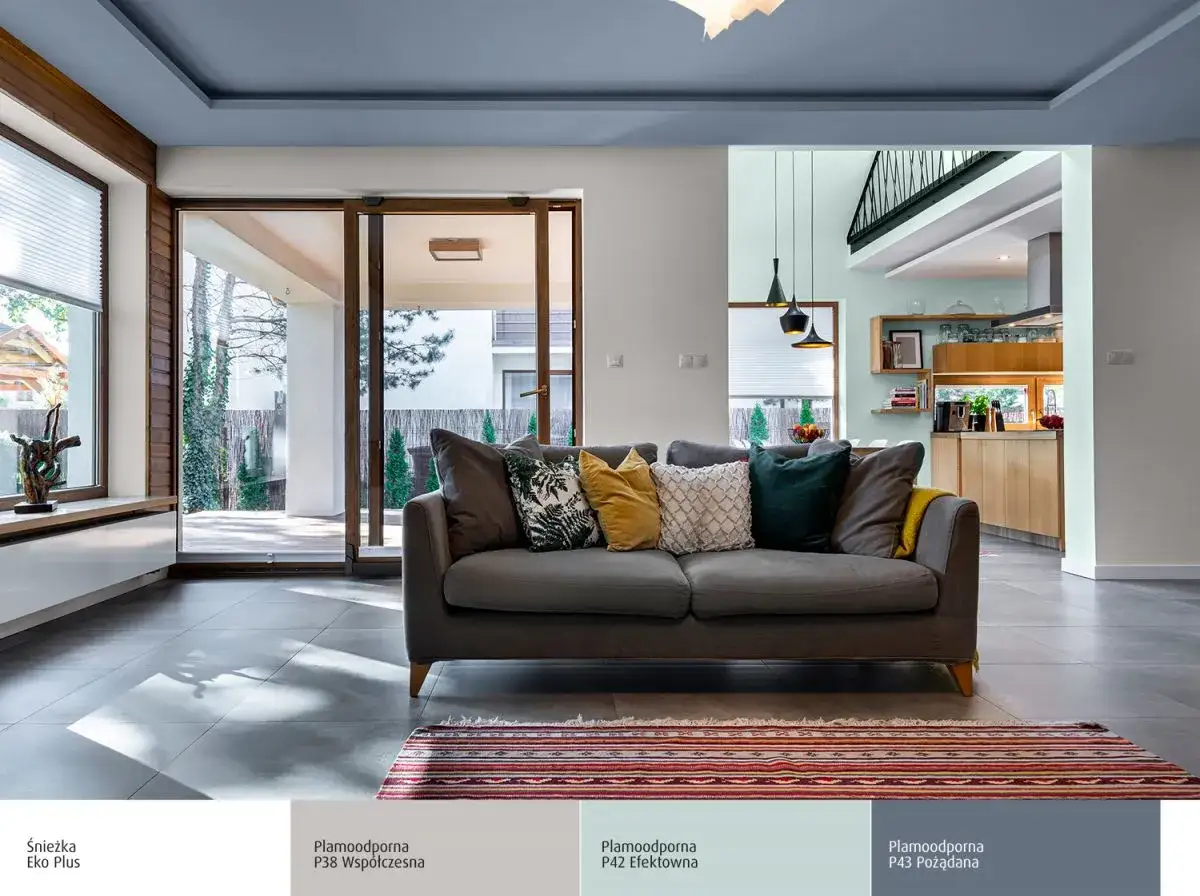 Inspiracja, jak pomalować ściany w salonie. Szara sofa, kolorowe poduszki i dywanik na tle jasnych ścian.