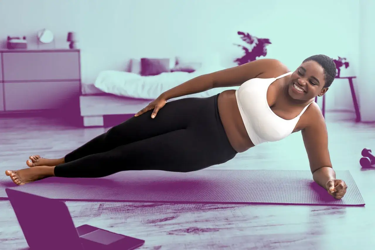 Uśmiechnięta kobieta wykonuje ćwiczenia na schudnięcie z brzucha w domu, ćwicząc deskę boczną na macie.