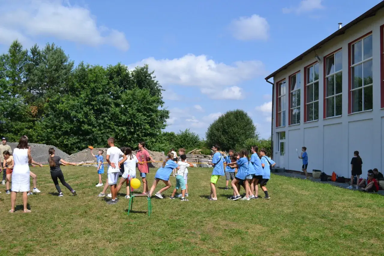 Dzieci grają w przeciąganie liny na trawie. Idealne miejsce, gdzie wysłać dziecko na obóz językowy, pełen aktywności i zabawy.